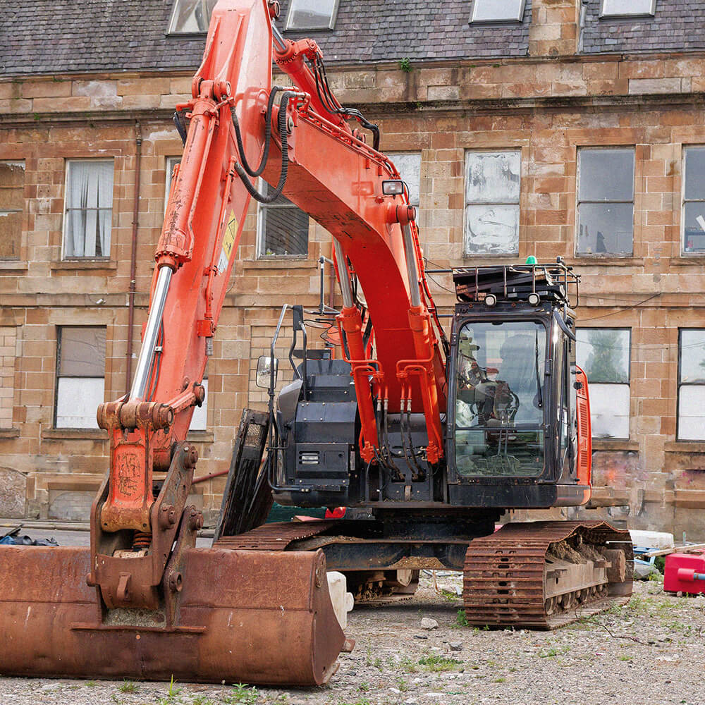 Excavator positioned in front of old buildings awaiting redevelopment