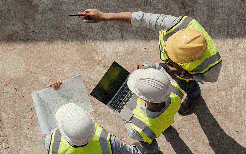 Developers wearing hard hats and high-visibility vests on construction site looking at plans